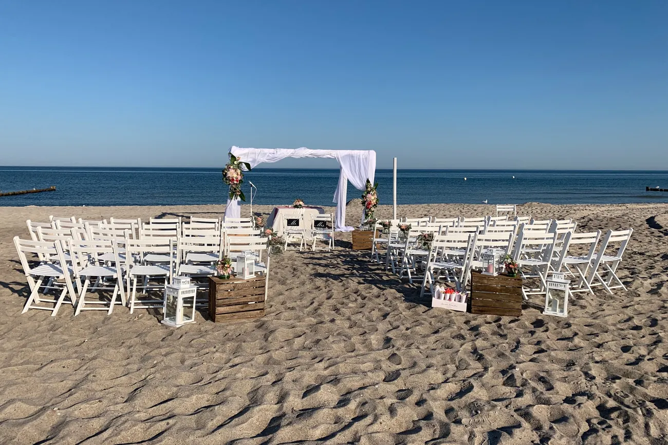 Trauungsbogen und weiße Stuhlreihen am Strand von Dierhagen
